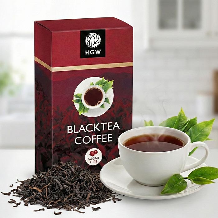 Taza de café con té negro HGW servido caliente junto a su caja y hojas de té naturales.
